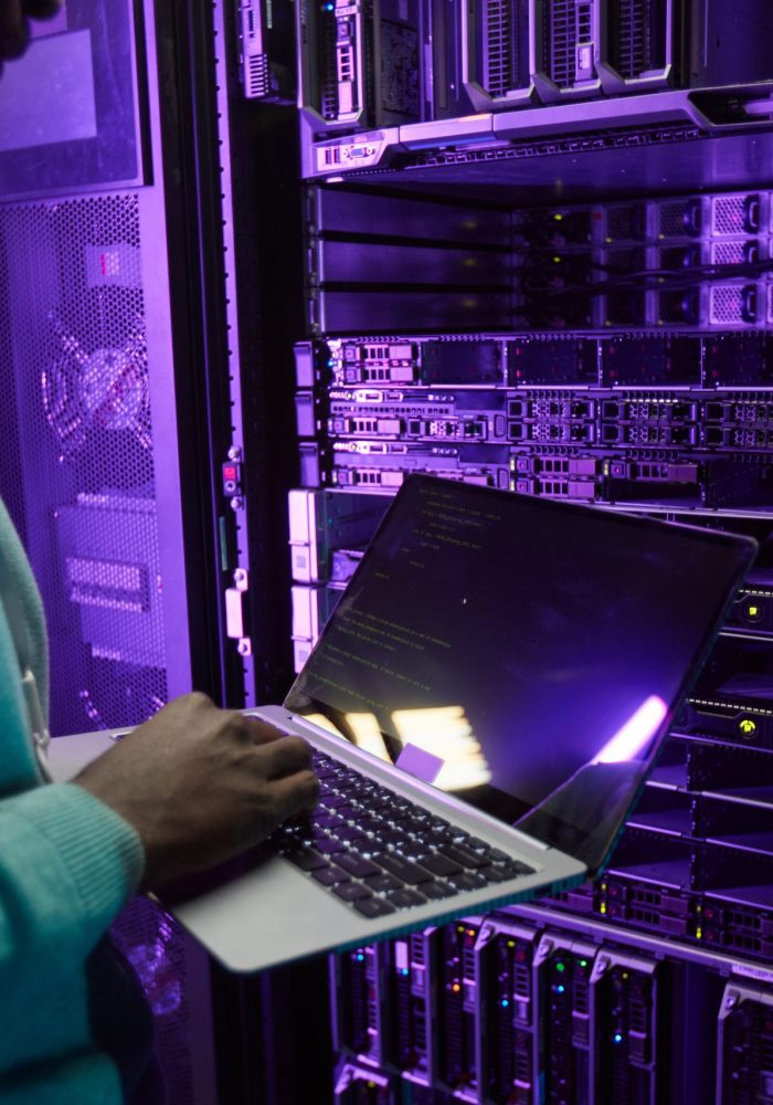 Cropped shot of African American data engineer holding laptop while working with supercomputer in server room lit by blue light, copy space
